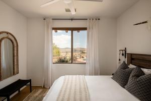 a bedroom with a white bed and a window at Saguaro Ridge by Fieldtrip Boulder Estate w Mtn Views Hot Tub Soaking Pool Yoga Deck in Yucca Valley +67 photos