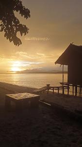 a picnic table and a hut on the beach at sunset at Blacktive Homestay in Kri