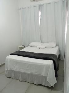 ein weißes Schlafzimmer mit einem Bett und weißen Vorhängen in der Unterkunft Hotel Tomazina in Tomazina