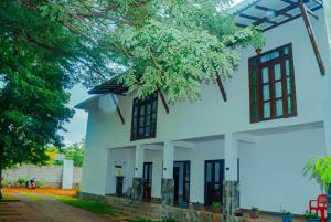 a white house with black windows and a tree at Nimala Holiday Homes in Mihintale
