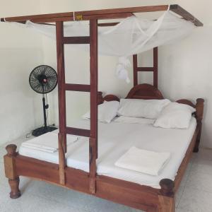 a wooden bunk bed with white sheets and a fan at Sancanka Nungwi in Nungwi