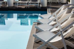 a row of white chairs next to a swimming pool at Hotel Juliani - Boutique Hotel in St. Julianʼs