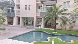 a swimming pool in front of a building with a palm tree at Apartamento JTR Maceio AL in Maceió