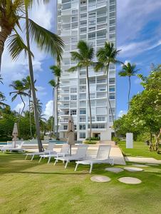a row of white benches in a park with a tall building at Caribbean Sea Breathless Views Apartment in La Puntica de Juan Dolio