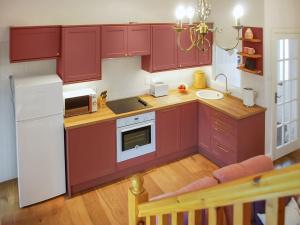 una cucina con armadi rossi e frigorifero bianco di School Cottage a West Burton