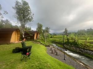 a woman sitting in a chair next to a river at Tranquil Riverside Camping in Ambengan