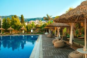 a resort with a swimming pool with straw umbrellas at Palmonte Suites Hotel & SPA in Kyrenia