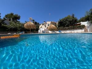 a swimming pool with blue water and straw umbrellas at Casa Palmerita a 7 minutos andando de una playa de aguas cristalinas in Teulada