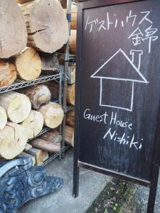 un cartello con la lavagna accanto a una pila di legno di Guesthouse Nishiki a Chichibu