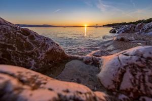 a sunset over a body of water with rocks at Apartment Di Novi Vinodolski in Novi Vinodolski