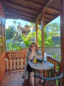 a woman sitting at a table on a porch at Mondok Dini in Ketewel