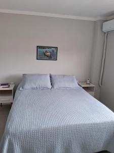 a white bed in a white bedroom with two tables at Apartamento novo entre a praia dos Ingleses e Santinho in Florianópolis