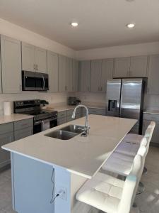 a kitchen with a sink and a counter with two white chairs at Modern Lux 3BR Home Near Disney and Lego Land! in Haines City