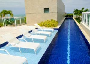 a swimming pool with white chairs next to a building at Apartamento JTR Maceio AL in Maceió +14 photos