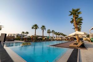 a large swimming pool with palm trees and umbrellas at Shades Beach Club in Jeddah