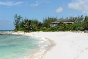 a white beach with a house in the distance at Alfred House home in Governorʼs Harbour