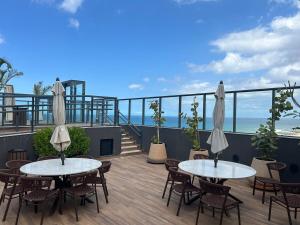 two tables and chairs on a balcony with the ocean at Studio beira mar próximo do centro de convenções em Armação in Salvador