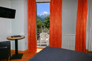 Cette chambre dispose d'une fenêtre avec des rideaux orange et d'une table. dans l'établissement Hôtel Panoramic, à Luchon