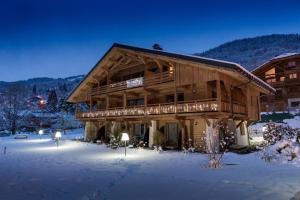 un grand bâtiment en bois dans la neige avec des lumières dans l'établissement Logis Hotel Gai Soleil, à Samoëns