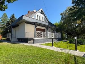 ein weißes Haus mit einer Veranda auf einem Rasen in der Unterkunft Ágica Nyaraló in Balatonkenese