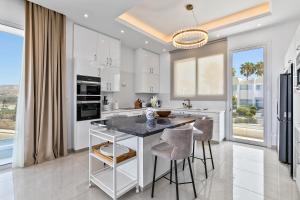 a kitchen with white cabinets and a table with stools at Olymp White Palace - The Ultra Luxury Beachfront House in Kissonerga