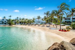 a beach with chairs and umbrellas and palm trees at Hodges Bay Resort & Spa, an HQ Luxury Resort & Residences in Saint Johnʼs