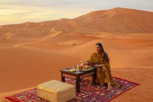 a woman sitting at a table in the desert at Sahara Family Luxury Camp in Merzouga