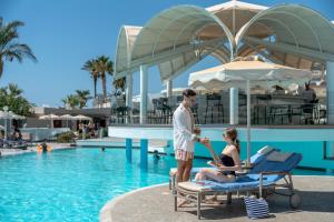 Ein Mann und eine Frau stehen neben einem Pool in einem Ferienresort. in der Unterkunft Rodos Palladium Leisure & Wellness in Faliraki