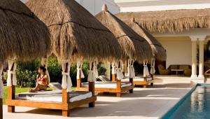a row of beds with straw umbrellas next to a pool at Grand Riviera Princess - All Inclusive in Playa del Carmen