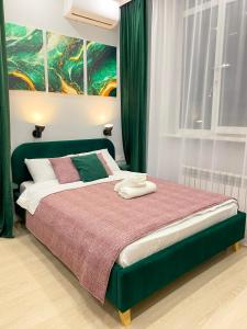 a bedroom with a green bed with a painting on the wall at Contento Apartments in Almaty