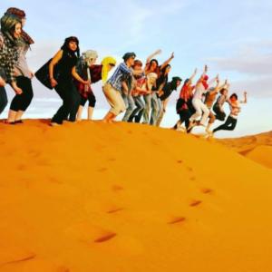 a group of people jumping on top of a sand mound at Merzouga tente luxury in Merzouga