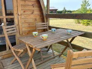 een houten tafel met kopjes en een stoel op een veranda bij Terres du Calvados 