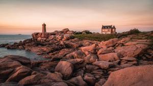 ein Haus an einer felsigen Küste mit einem Leuchtturm in der Unterkunft Les agapanthes in Perros-Guirec