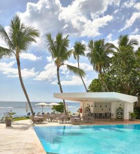 a pool with chairs and palm trees next to the ocean at Beachfront FL21 Con Tina Aquarella in La Puntica de Juan Dolio