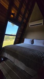 a bedroom with a large bed with a large window at Araucária Guest House - Cabanas in Bocaina de Minas