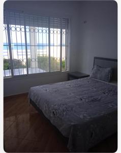 a bedroom with a bed and two large windows at Villa Sounine in Raʼs al Jabal