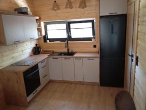 a kitchen with white cabinets and a black refrigerator at Dadaj Chill 2 domek nad jeziorem, wanna jakuzzi, fotel masujący in Wilimy