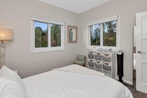 a white bedroom with a bed and two windows at Chic Whangarei Retreat - 10 min Walk to CBD in Whangarei