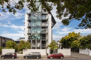 a tall white building with cars parked in a parking lot at Stylish City Apartment with Balcony and Parking in Christchurch