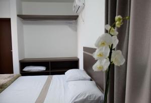 a bedroom with a bed and a vase with white flowers at Suítes Trindade in Florianópolis