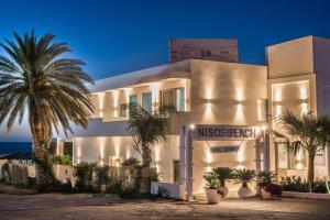 a building with a palm tree in front of the ocean at Drossia Palms Hotel and Nisos Beach Suites in Malia