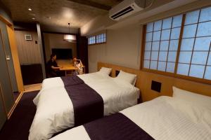 two beds in a room with two people sitting at a table at Hotel Matsunoi Shurin in Tokyo