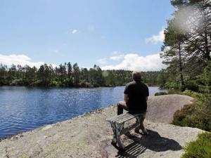 a man sitting on a bench looking at a lake at 8 person holiday home in Kvås in Kvås