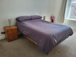 a bed with a purple comforter and a night stand at Central 2-bedroom bunglow with double sofa bed in Carnoustie