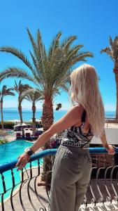 eine Frau steht neben einem Zaun mit Palmen in der Unterkunft New Sphinx Resort in Dahab