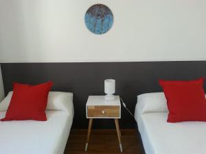 two beds in a room with red pillows and a night stand at Malhara in Seville