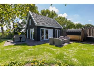 Un pequeño cobertizo negro con sillas y césped. en Family house with an ideal location, private terrace, garden and sauna, en Vrouwenpolder
