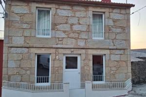 a stone building with a white door and windows at A de Laura in Lariño