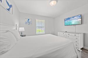 a white bedroom with a bed and a flat screen tv at Tranquil Haven - Pet Friendly in Perdido Key