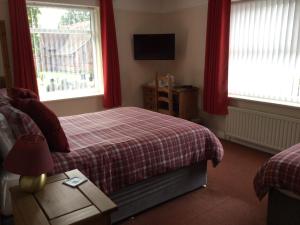 a bedroom with a bed and two windows with red curtains at Gateway Lodge in Speke